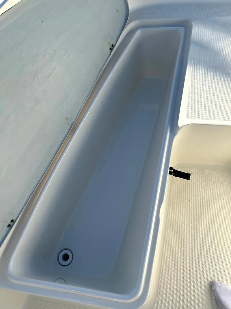 Slide: The Image of 2003 Pursuit 2470 Center Console boat storage compartment, open lid, white interior. - 9