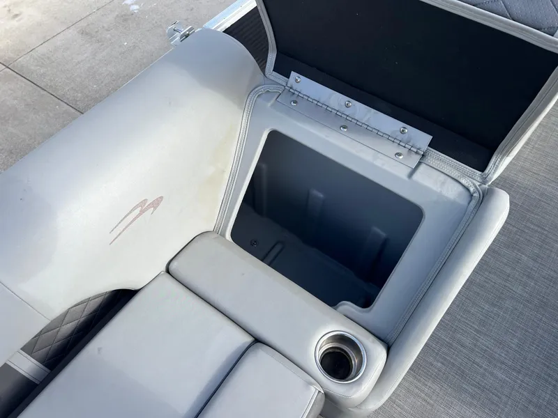 Slide: The Image of 2021 Bennington L 21 Swingback seat storage compartment with cup holder, open on a boat deck. - 21