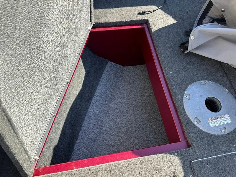 Slide: The Image of 2015 Lund 1750 Rebel XS SS boat storage compartment with red trim and gray carpet. - 29