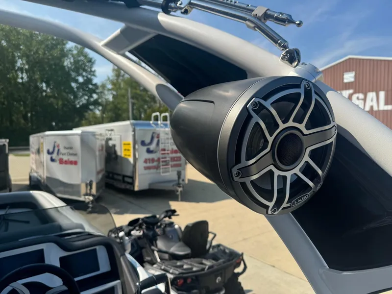 Slide: The Image of 2024 Manitou 27 XT RFXW boat with mounted speaker, trailers in background. - 15