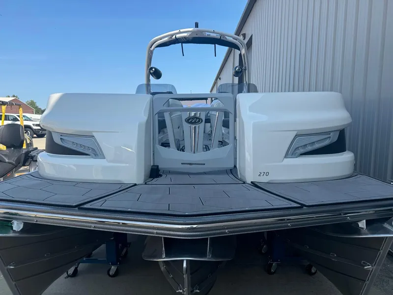 Slide: The Image of 2024 Manitou 27 XT RFXW pontoon boat, rear view, docked near a metal building. - 4