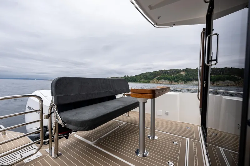 Slide: The Image of Nimbus C11 2022 boat deck with seating and table, overlooking serene waters and lush coastline. - 25