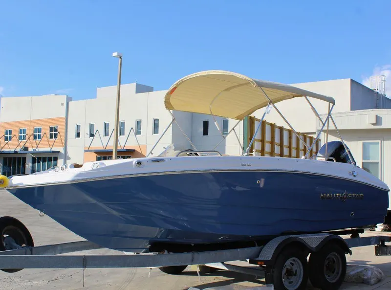 Slide: The Image of 2024 NauticStar 193 SC boat on trailer with canopy, parked outdoors. - 2