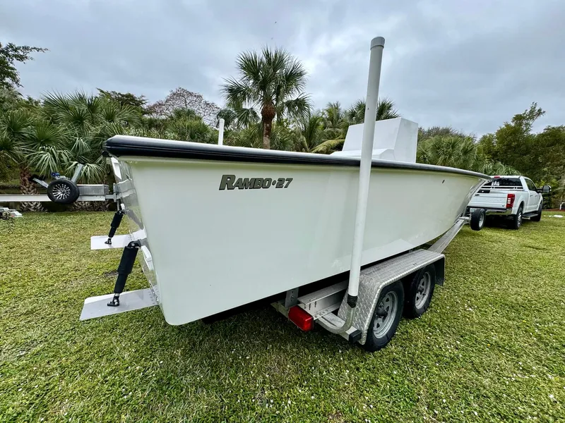 Slide: The Image of 2025 Rambo 27 boat on trailer, parked on grass with trees in background. - 2