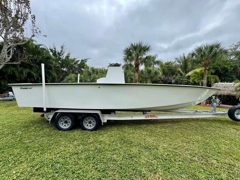 Slide: The Image of 2025 Rambo 27 boat on trailer, parked on grass with palm trees in background. - 9