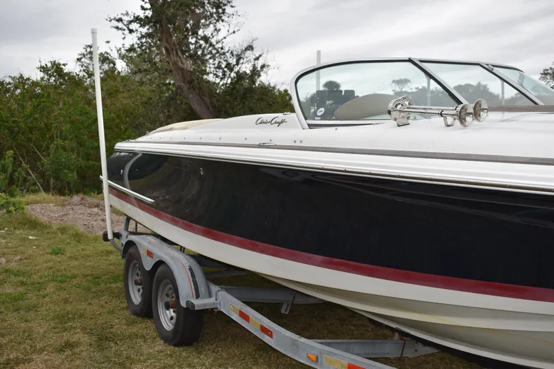 Slide: The Image of 2009 Chris-Craft Corsair 25 boat on trailer, black hull, parked on grass. - 4