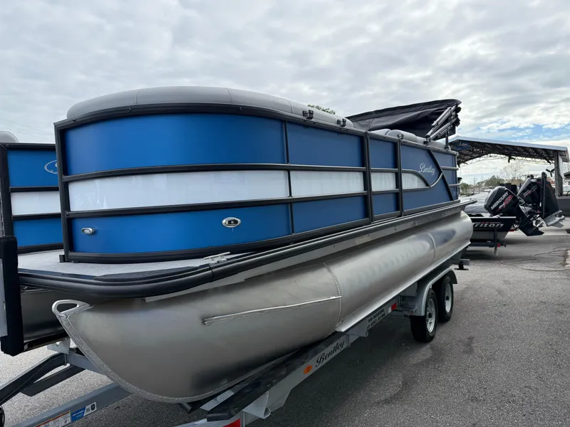 Slide: The Image of 2025 Bentley Pontoons 20 Legacy on trailer, blue and silver design, parked outdoors. - 5