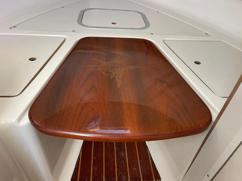 Slide: The Image of 2003 Pursuit 2870 Walkaround boat interior with wooden table and storage compartments. - 33
