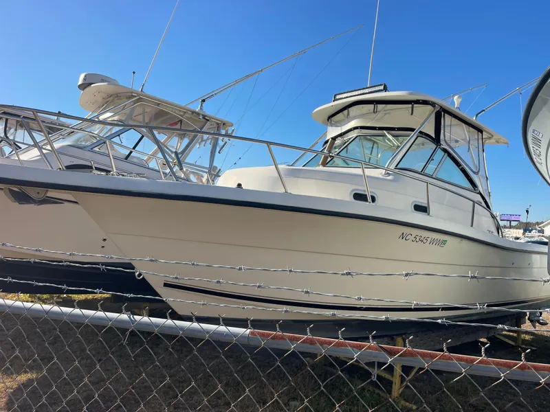 Slide: The Image of 2003 Pursuit 2870 Walkaround boat displayed behind a fence under clear blue sky. - 5