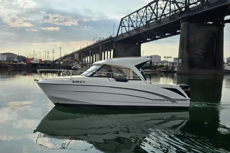Slide: The Image of 2022 Beneteau Antares 7 boat cruising under a bridge on calm waters. - 2