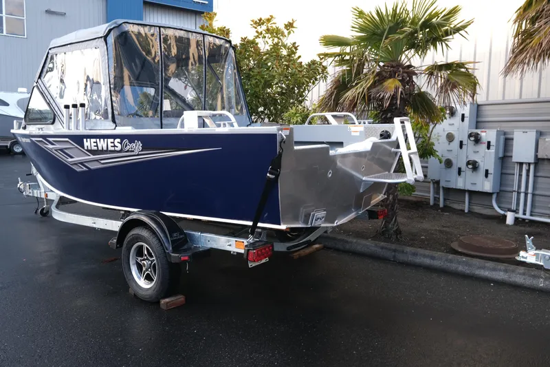 Slide: The Image of 2025 Hewescraft 180 Sportsman boat on trailer, parked outdoors near palm trees. - 4