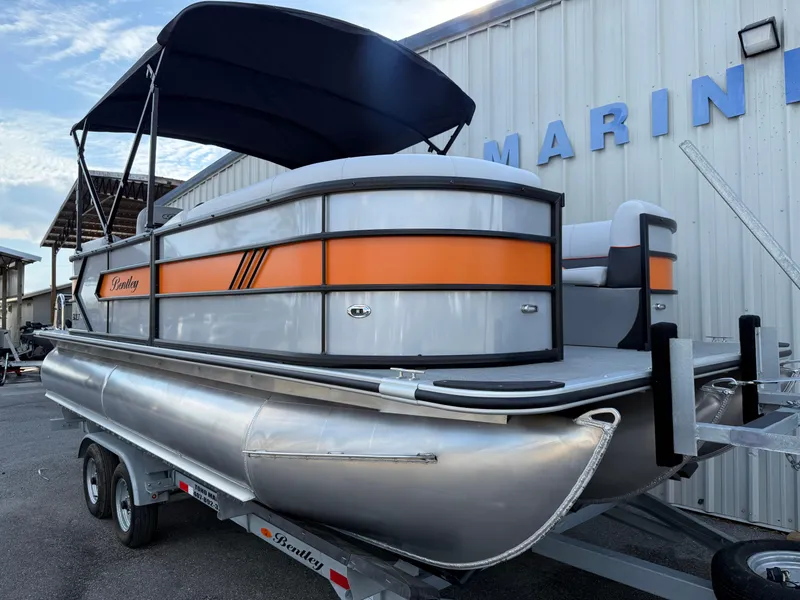 Slide: The Image of 2025 Bentley Pontoons Bolt 203 with orange accents on a trailer, docked at a marina. - 12