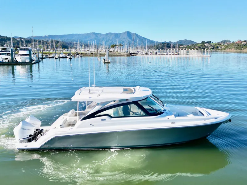 Slide: The Image of 2025 Tiara Yachts 34 LX cruising in a scenic marina with mountains in the background. - 2