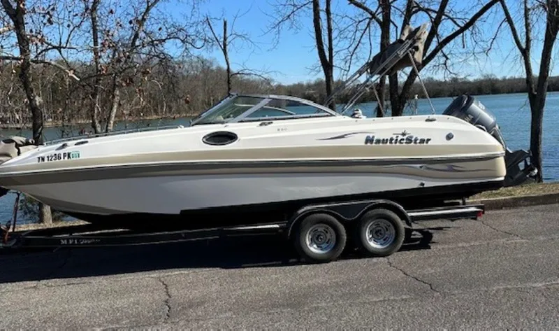 The Image of 2010 NauticStar 230DC Sport Deck boat on trailer by a lake. - 0