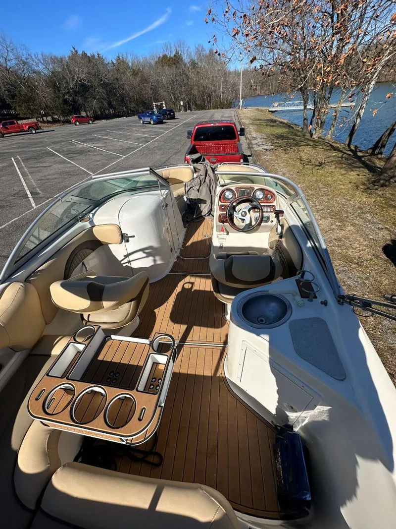 Slide: The Image of 2010 NauticStar 230DC Sport Deck boat with spacious seating and wood finish, parked near a lake. - 12