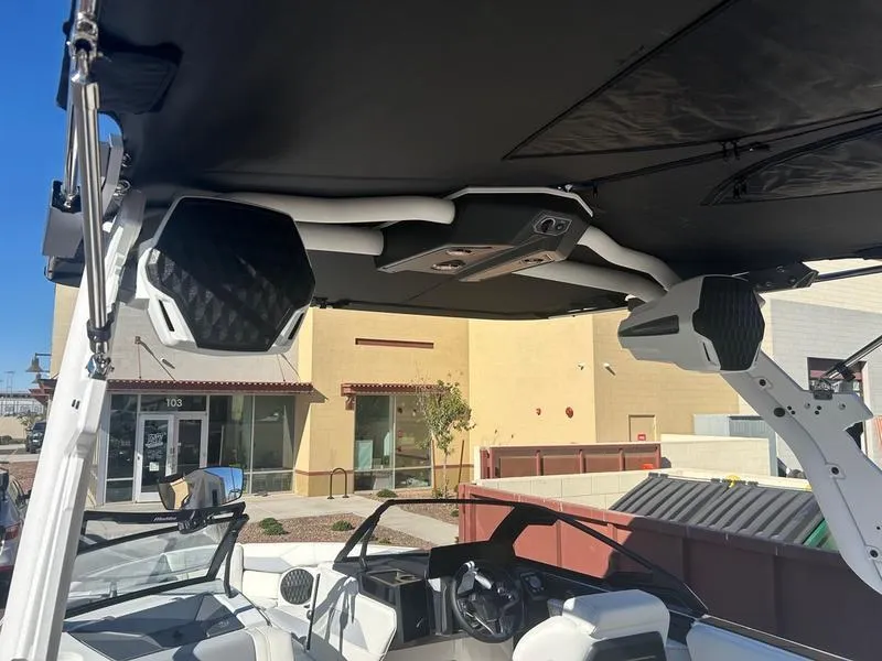 Slide: The Image of 2025 Malibu 23 LSV boat interior with speakers and canopy, parked near buildings. - 14