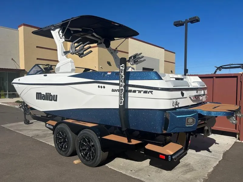 Slide: The Image of 2025 Malibu 23 LSV boat on trailer, white and blue design, parked outdoors. - 4