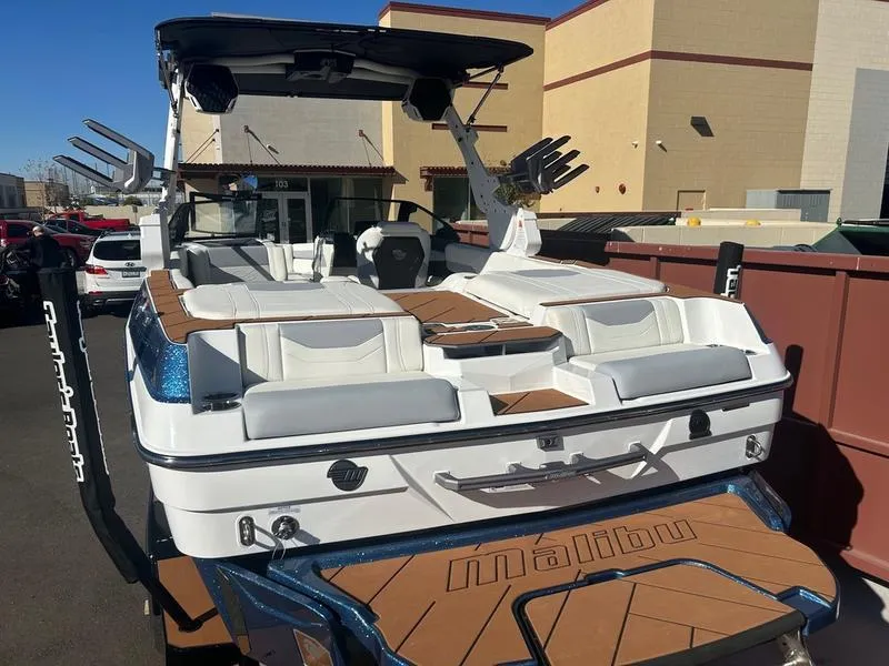 Slide: The Image of 2025 Malibu 23 LSV boat with white seating and brown deck, parked outdoors. - 9