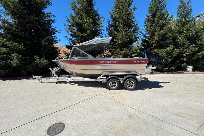 Slide: The Image of 2025 Spartan 185 Astoria boat on trailer, parked outdoors with trees in background. - 1