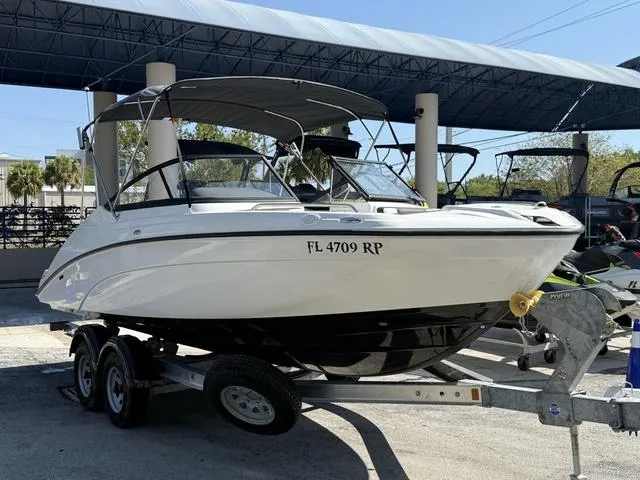Slide: The Image of 2018 Yamaha Boats SX210 on trailer, parked outdoors, with a building in the background. - 1