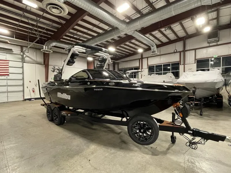 Slide: The Image of 2025 Malibu 23 LSV boat in a warehouse, sleek black design on a trailer. - 5