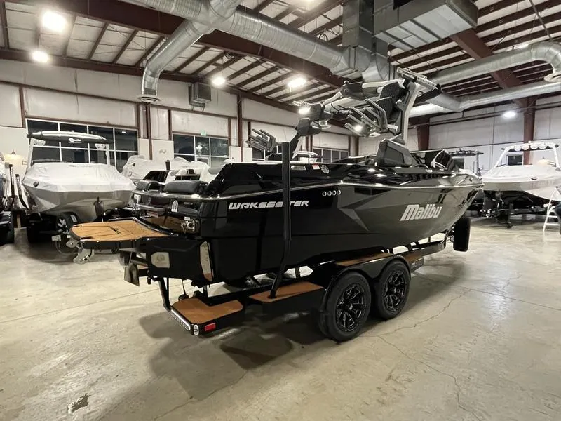 Slide: The Image of 2025 Malibu 23 LSV boat in showroom, black exterior, on trailer, surrounded by other boats. - 7