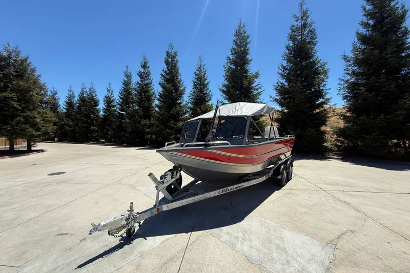 Slide: The Image of 2025 Spartan 200 Astoria boat on trailer, parked outdoors with trees in background. - 6