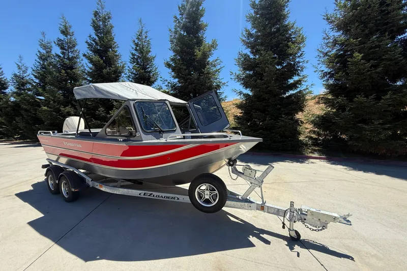 Slide: The Image of 2025 Spartan 200 Astoria boat on trailer, parked outdoors with trees in background. - 3