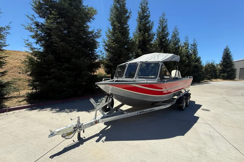 Slide: The Image of 2025 Spartan 200 Astoria boat on trailer, parked outdoors near trees. - 2