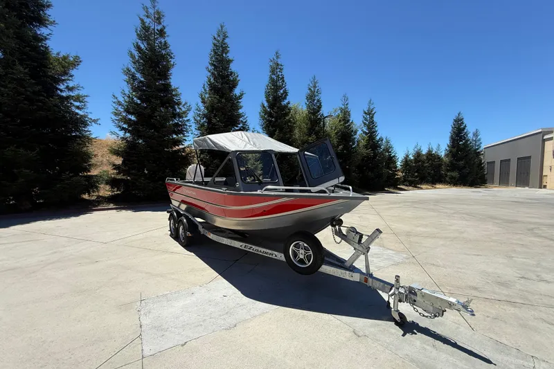 Slide: The Image of 2025 Spartan 200 Astoria boat on trailer, parked outdoors with trees in background. - 8