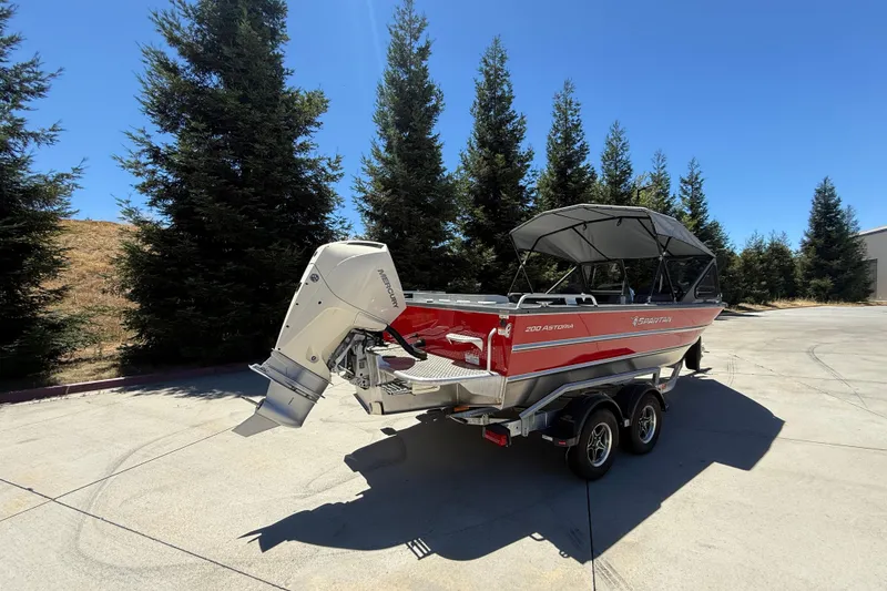 Slide: The Image of 2025 Spartan 200 Astoria boat with Mercury engine on trailer, surrounded by trees. - 4