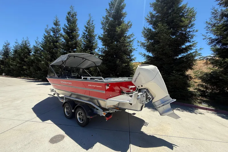 Slide: The Image of 2025 Spartan 200 Astoria boat on trailer, parked near trees under clear blue sky. - 7