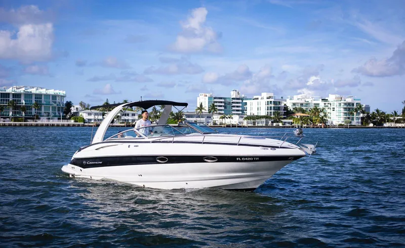 Slide: The Image of 2006 Crownline 320 LS boat cruising on a sunny day near modern waterfront buildings. - 1
