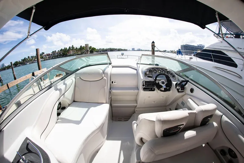 Slide: The Image of 2006 Crownline 320 LS boat interior with white seating, steering wheel, and dashboard, docked by the water. - 26