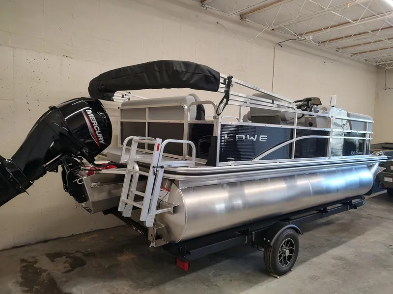 Slide: The Image of 2025 Lowe UC180 pontoon boat with Mercury outboard motor, parked indoors on a trailer. - 4