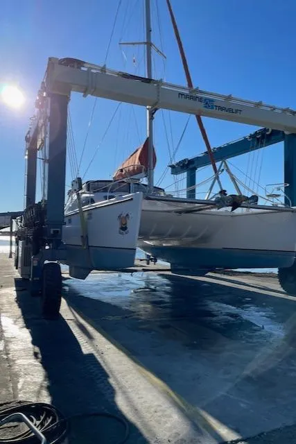 Slide: The Image of Sailboat Voyage Maxim 2001 being lifted by a marine travel lift under clear blue sky. - 16