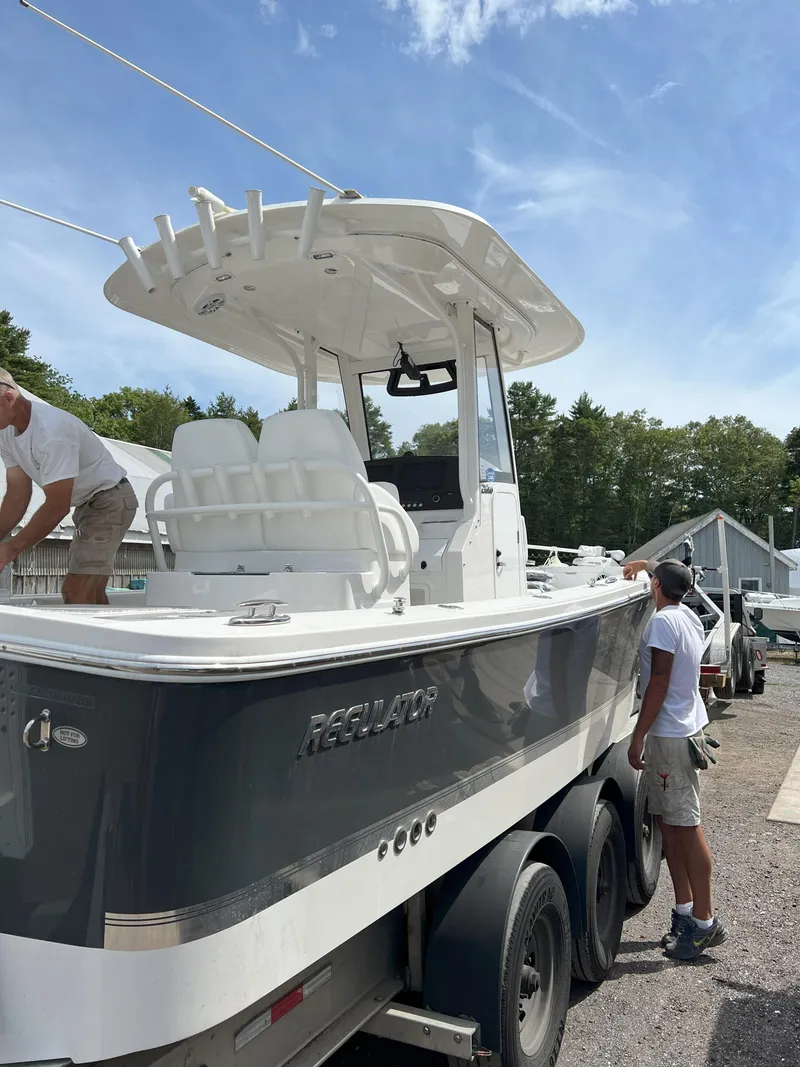 Slide: The Image of 2021 Regulator 26XO boat on trailer, with people inspecting it outdoors. - 13