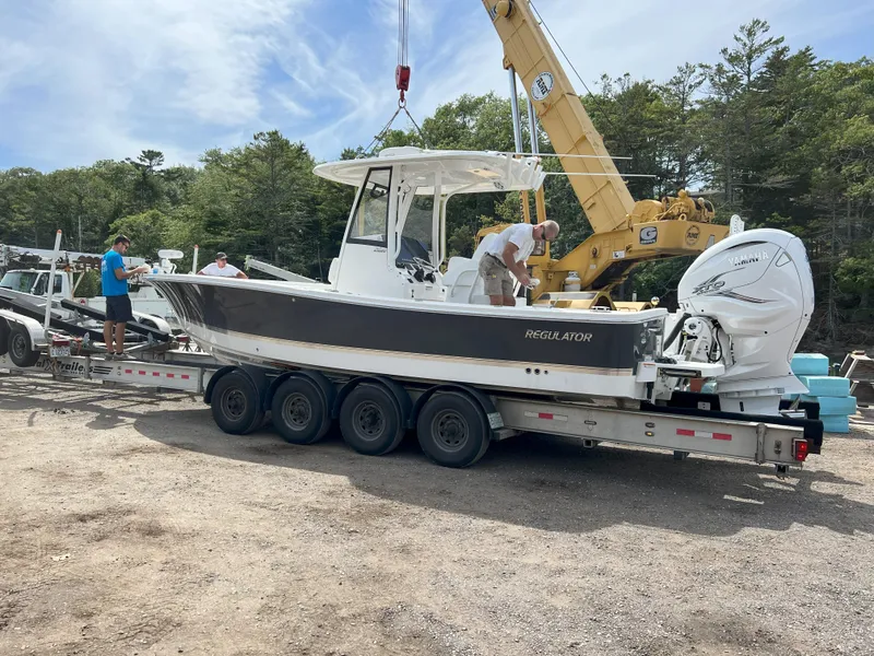 Slide: The Image of 2021 Regulator 26XO boat on trailer, with people inspecting, surrounded by trees and machinery. - 15