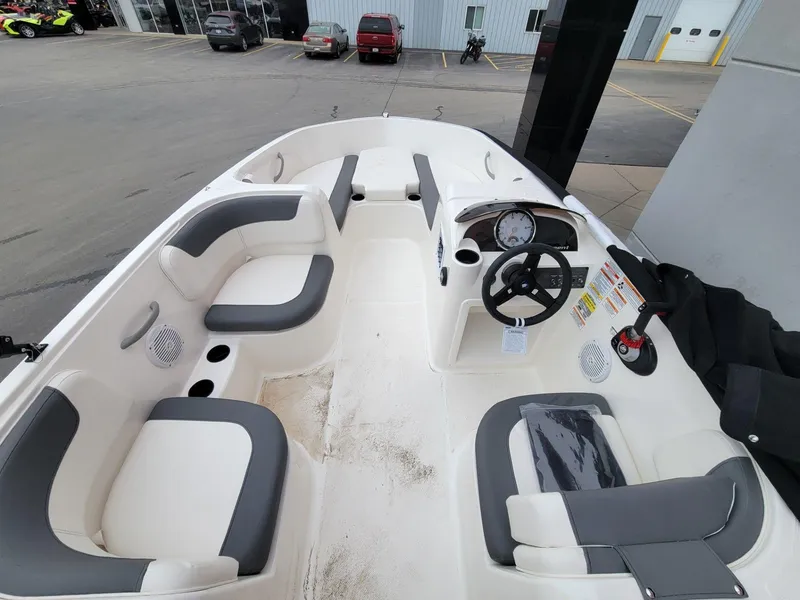 Slide: The Image of 2025 Bayliner Element E18 boat interior with seating and steering wheel, parked at a dealership. - 14