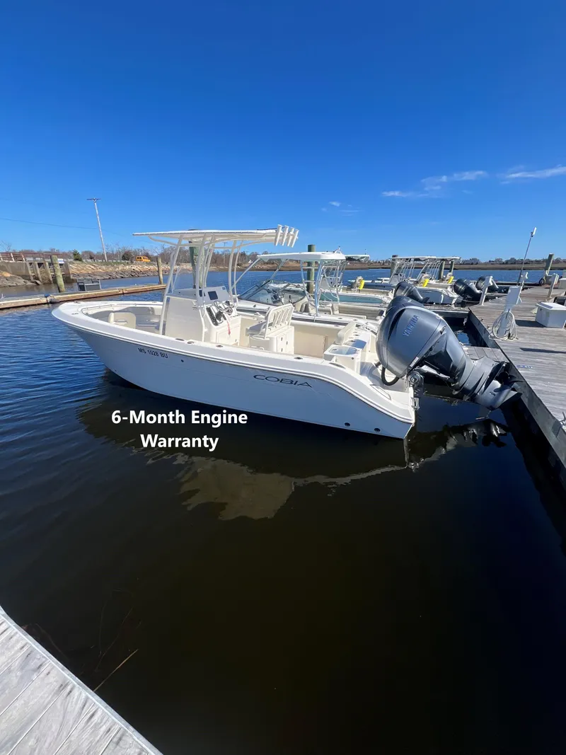 Slide: The Image of 2023 Cobia 237 CC boat docked, featuring a 6-month engine warranty. - 0