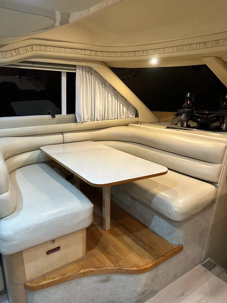 Slide: The Image of 2000 Sea Ray 480 Sedan Bridge interior with beige seating and wooden table. - 8