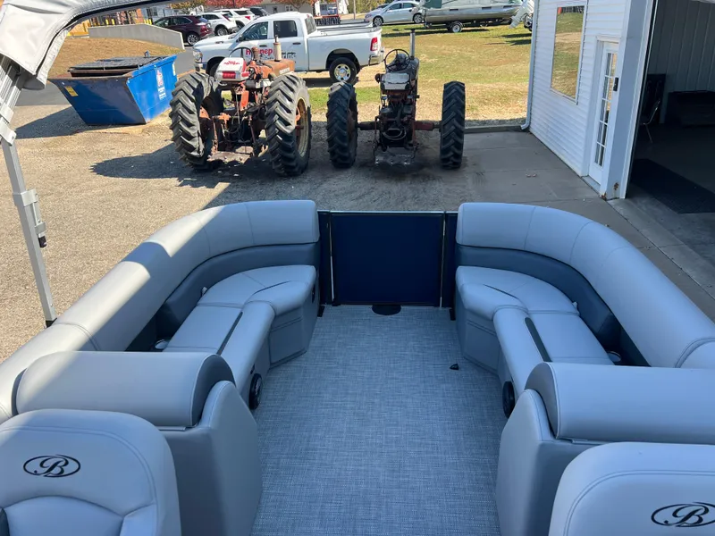 Slide: The Image of 2025 Bentley Pontoons Legacy 243 Navigator interior with plush seating, parked near tractors. - 16