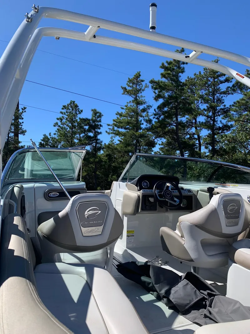Slide: The Image of 2023 Crownline E235XS boat interior with seating and steering wheel, set against a forest backdrop. - 5