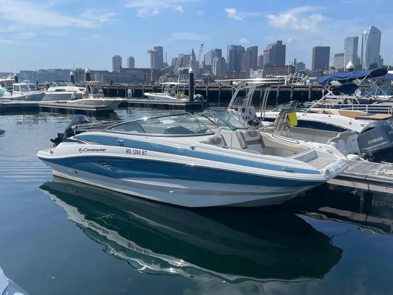 Slide: The Image of 2022 Crownline E235XS boat docked in a marina with city skyline background. - 2