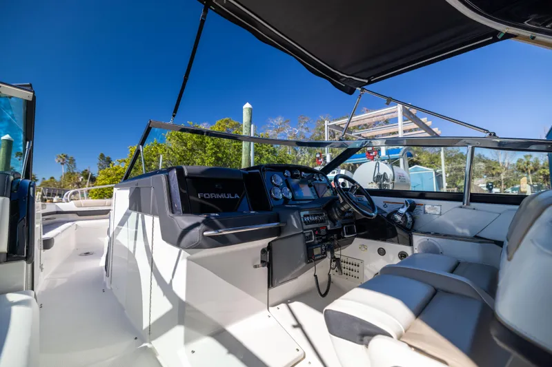 Slide: The Image of 2017 Formula 330 Crossover Bowrider interior with helm, seating, and canopy under clear blue sky. - 23