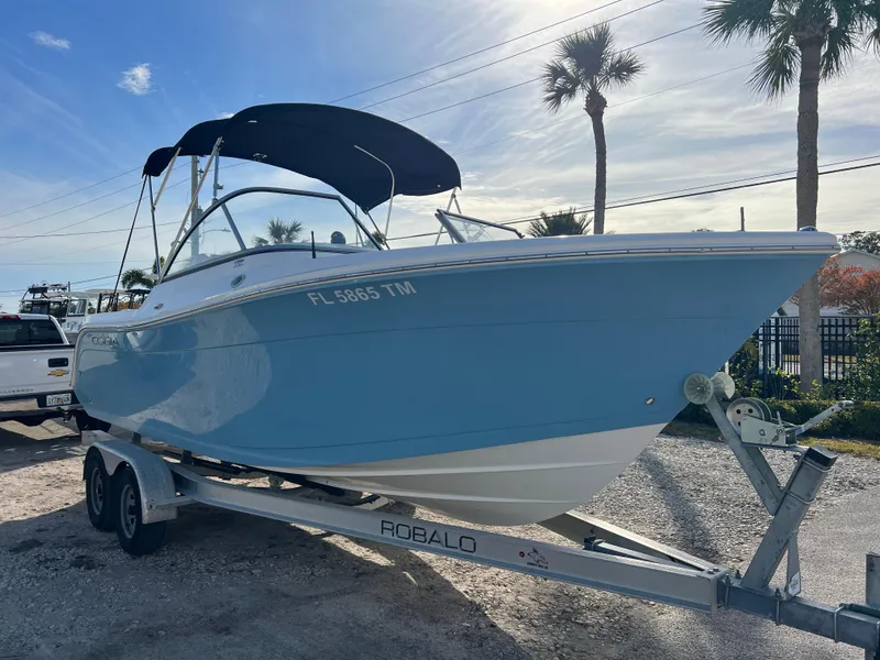 Slide: The Image of 2023 Cobia 220 Dual Console boat on trailer, blue hull, parked outdoors. - 1