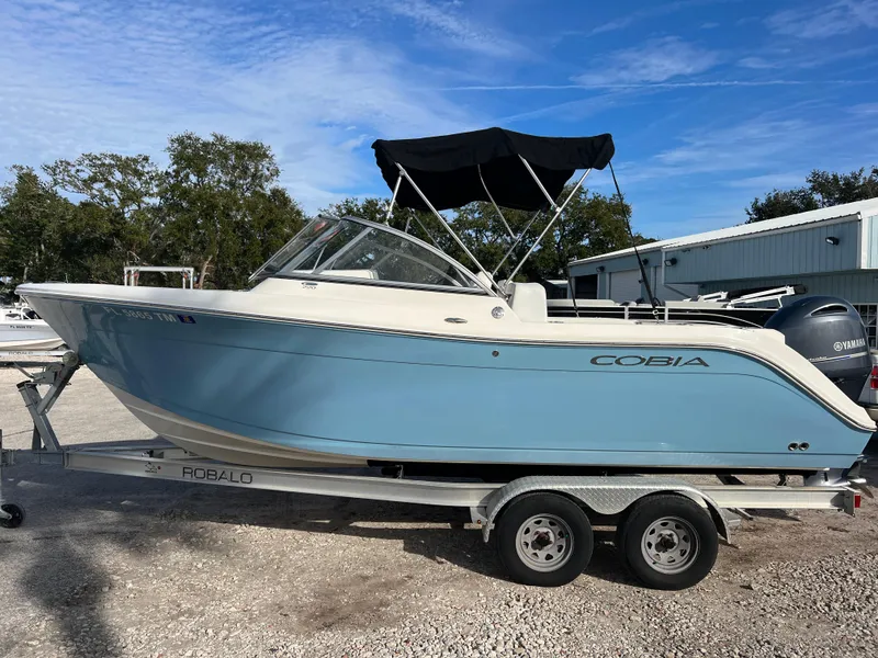 Slide: The Image of 2023 Cobia 220 Dual Console boat on trailer, blue hull, parked outdoors. - 4