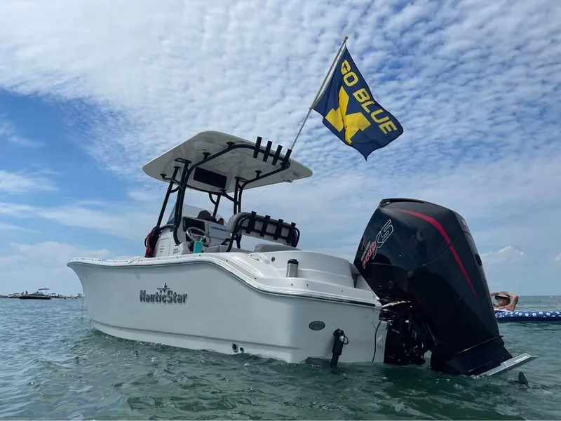 Slide: The Image of 2022 NauticStar 2302 Legacy boat with flag, anchored in calm waters under a blue sky. - 11