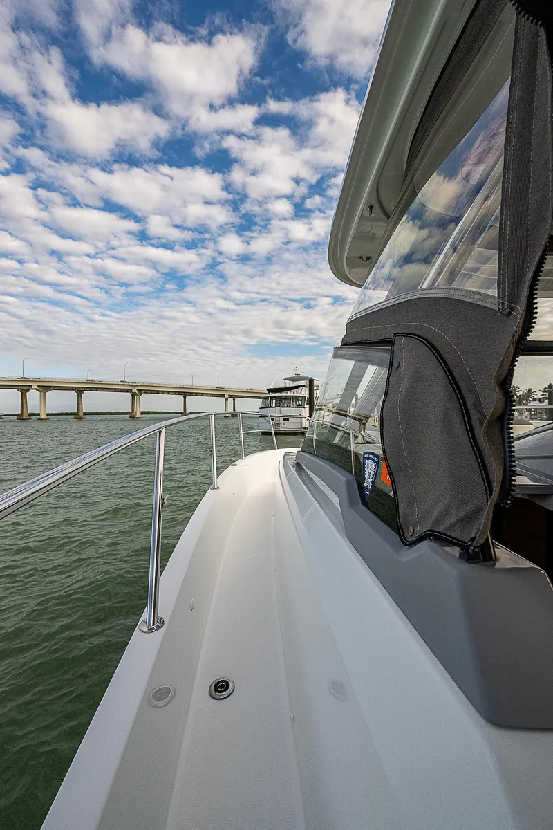 Slide: The Image of 2022 Jeanneau Leader 12.5 yacht cruising near a bridge under a partly cloudy sky. - 18