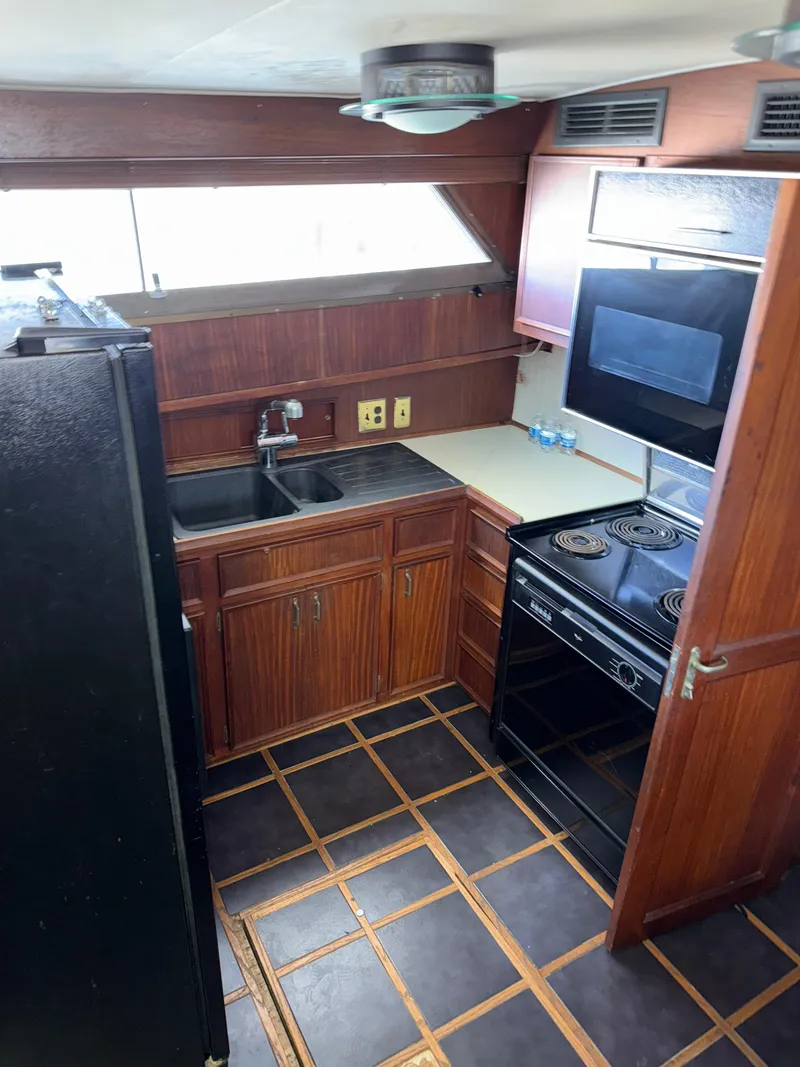 Slide: The Image of 1980 Hatteras 58MY yacht kitchen with wood cabinetry, black appliances, and tiled flooring. - 10